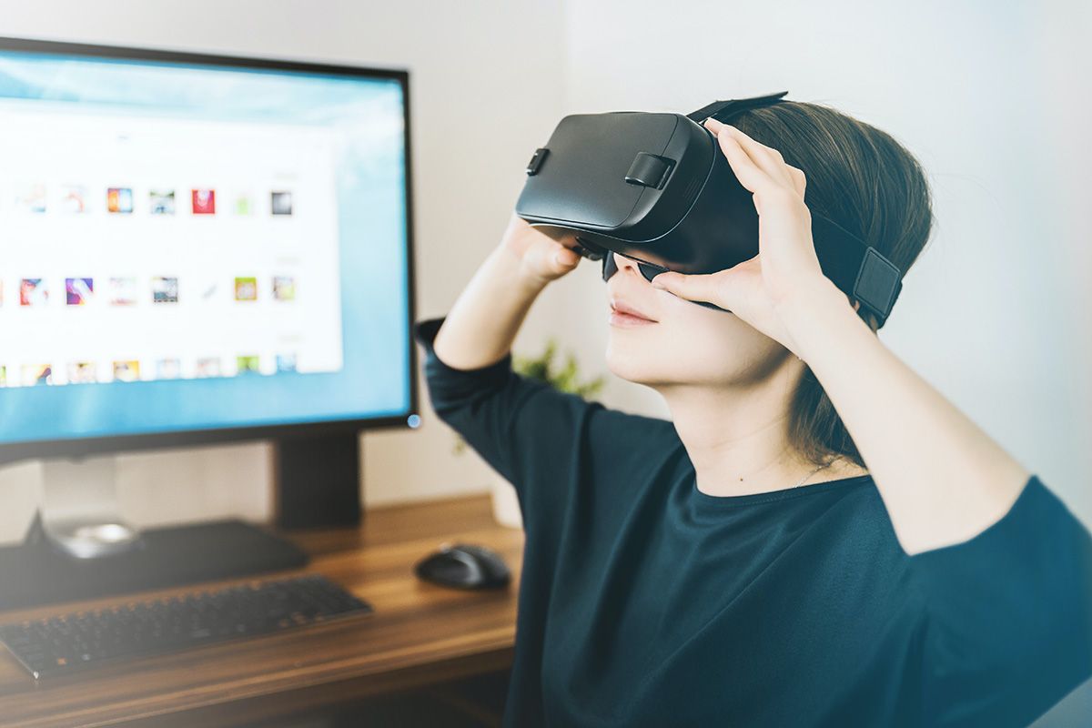 Woman sitting in front of a computer monitor and wearing a VR headset